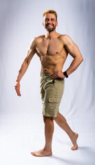 Fototapeta premium muscular man in shorts posing, shows, straining muscles. gray background