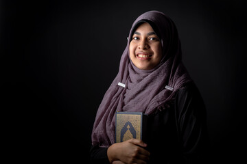 Portrait Asian Muslim woman standing and reading the Quran and appreciates and faith The Holy Al Quran with written Arabic calligraphy meaning of Al Quran, Arabic word translation: The Holy Al Quran.