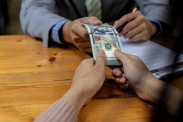 Picture of two people handing over a dollar, they are business partners who are doing corrupt behavior by bribing them for illegal mutual benefit. The concept of business fraud and bribery.