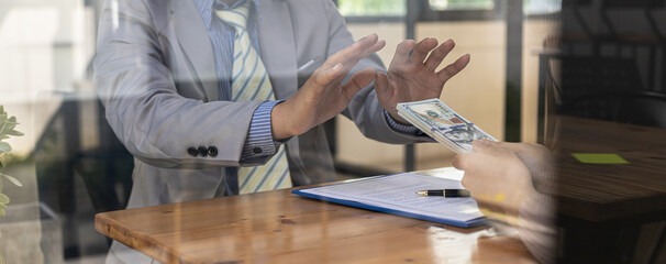 Two people are doing corrupt behavior, they are mutual business partners and are trying to bribe money while one person is refusing to accept the bribe. Business fraud and bribery an illegal concepts.