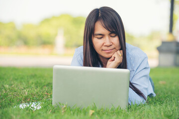 Asian woman lay down green garden park using laptop working outdoor home office. Happiness Woman smile working Freelance on laptop. Young Women University student type computer laptop at green nature