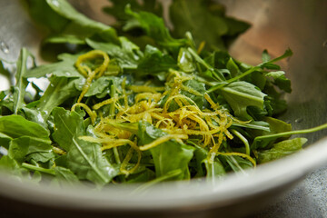 Salad with arugula and orange zest in metal bowl