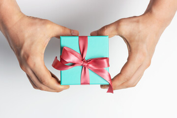 Male hands holding gift box with ribbon on white background, top view