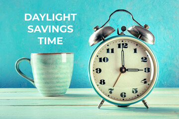 Daylight Saving Time concept. A retro alarm clock with a cup of coffee on a teal background