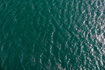 bewegte Wasseroberfläche mit Wellen und Gischt eines Sees im Sonnenlicht von oben