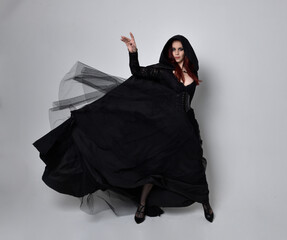 Full length portrait of dark haired woman wearing  black victorian witch costume with a flowing ...