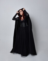 Full length portrait of dark haired woman wearing  black victorian witch costume with a flowing ...