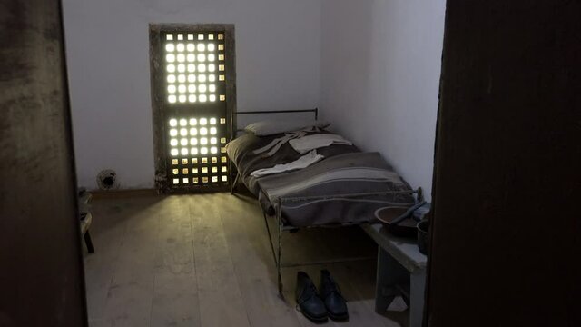 19th century prison cell with barred window, bed and personal items.