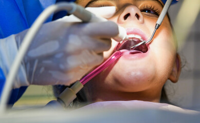 Young caucasian female with dentist in white latex gloves check condition of her teeth. baby girl in blue dental chair.
