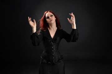 close up portrait of red haired woman wearing  black victorian witch costume.  standing pose, with ...