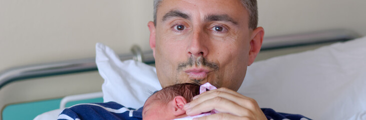Happy man holding his newborn baby at the hospital. Life and family concept