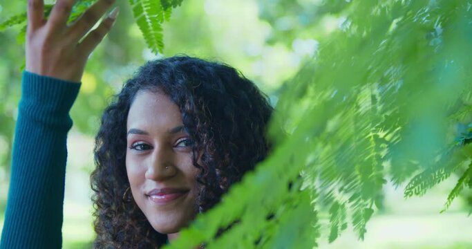 A young girl lifts tree branches to reveal her pretty face
