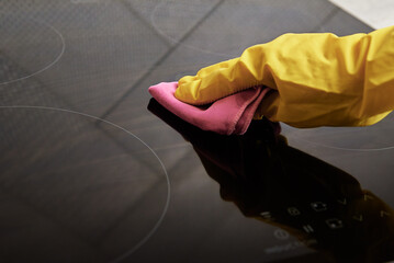 Cleaning induction stove. Woman in yellow rubber gloves cleans kitchen induction hob with cleaning...