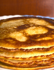 Golden pancakes lie on top of each other on a closeup plate.