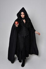 Full length portrait of dark haired woman wearing  black victorian witch costume  standing pose, with  gestural hand movements,  against studio background.