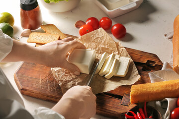 Woman cutting feta cheese on table in kitchen