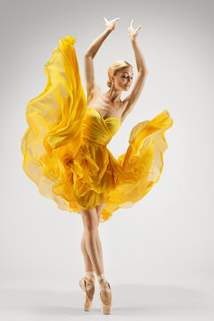 Fototapeta Dancing Woman in Yellow Dress. Ballerina in Shoes Dance Modern Art Ballet over Light Gray Background. Graceful Girl Stretching Hands up