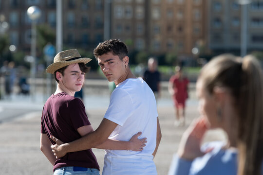 Gay angry teenager couple looking back to surprised woman. Homophobia in adolescence concept.