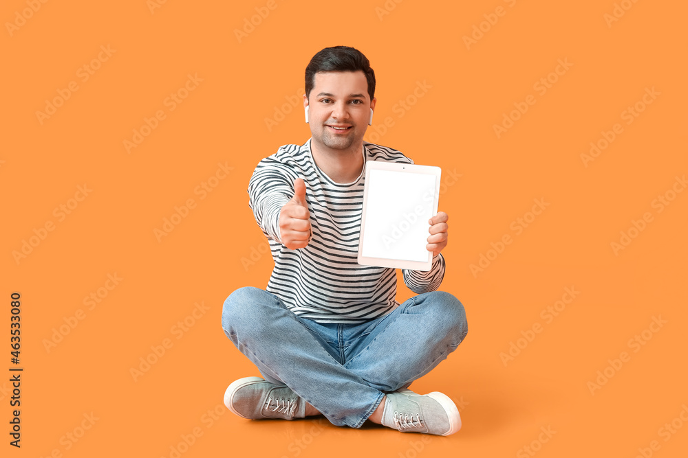 Poster young man with tablet computer and earphones showing thumb-up on color background