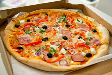 Pizza with bacon, cheese, olives, herbs and bell pepper lying on a paper package.