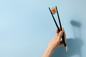Woman holding chopsticks with delicious salmon maki roll on color background