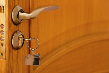 Opened door with handle and key with keychain in modern lock, closeup