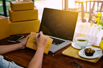 Hands of a working woman writing a list of shipping addresses for customers. Freelance business and online shopping, work at home concept.