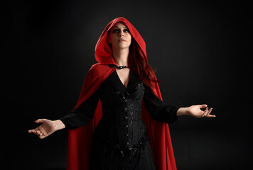 close up portrait of girl wearing red riding hood cloak and witch costume, isolated on black studio...