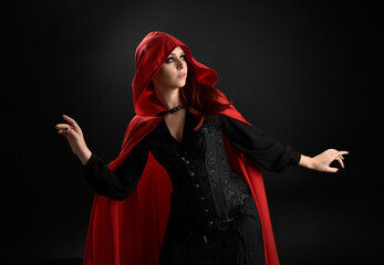 close up portrait of girl wearing red riding hood cloak and witch costume, isolated on black studio...