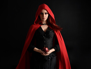 close up portrait of girl wearing red riding hood cloak and witch costume, isolated on black studio...