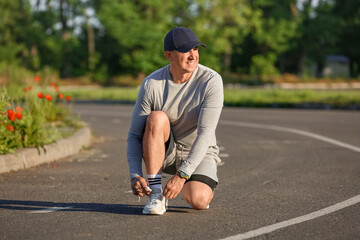 Sporty mature man tying shoe laces on road