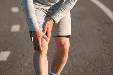 Sporty mature man suffering from knee pain after running outdoors