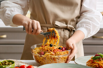 Woman preparing tasty Pasta Puttanesca at table in kitchen, closeup