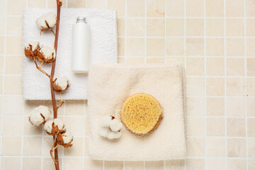 Clean towels, bottle of cosmetic product, massage brush and cotton branch on light tile