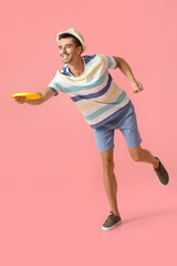 Handsome young man throwing frisbee on pink background