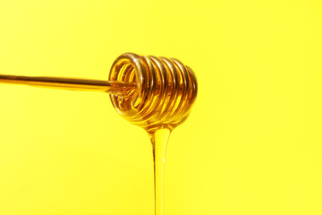 Pouring of tasty honey from dipper on color background, closeup
