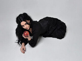 Full length portrait of dark haired woman wearing  black victorian witch costume,  lying on the...