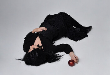 Full length portrait of dark haired woman wearing  black victorian witch costume,  lying on the...