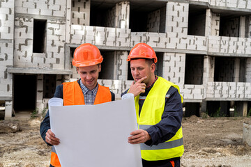 two workers in overalls and helmets stand near the new building and talk