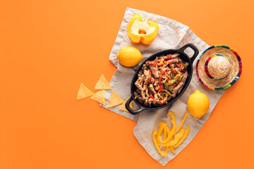 Frying pan with tasty Fajita, nachos and sombrero hat on color background