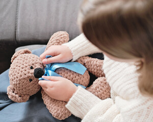 little girl playing with knitted teddy bear and ties a ribbon or bow. Top view, unrecognizable person. knitting as hobby, hand made toys