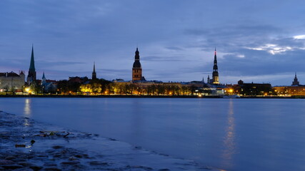 Fototapeta premium Autumn dawn in blue tones over old Riga reflection of night lights in the Daugava