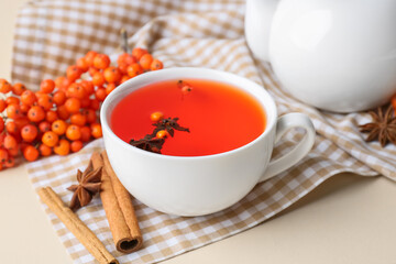 Cup of delicious rowan tea and spices on color background