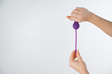 A faceless woman holding an electronic Kegel trainer for training pelvic floor muscles on a white...