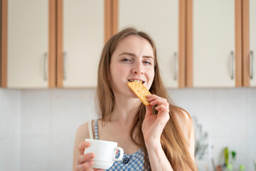 Young woman bites cracker and slyly looks at camera. Girl drinks coffee and eating cookies. Cheat...