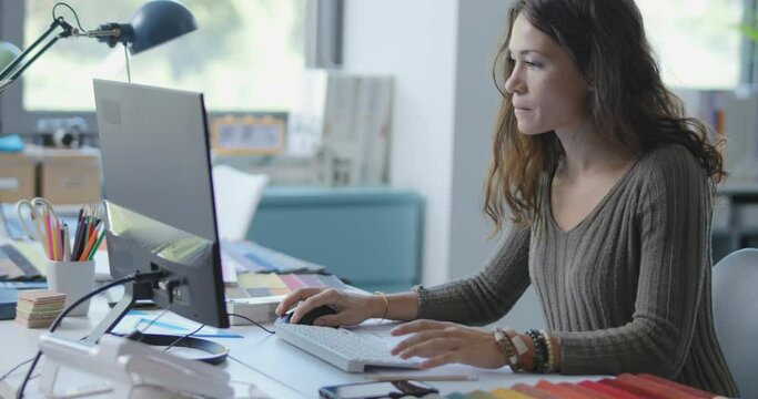 Young interior designer working in her studio, she is choosing fabric swatches and using her computer
