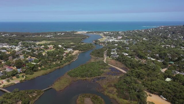 Slow aerial flight along natural Anglesea River to ocean beach beyond