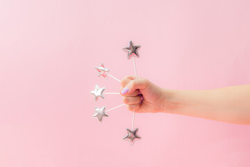 Beautiful female hand hold five silver toy stars on the stick. Pink pastel background.