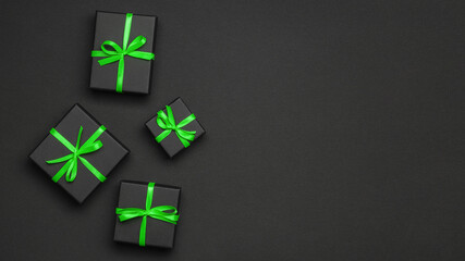 Black gift boxes tied with green ribbons on a black background.