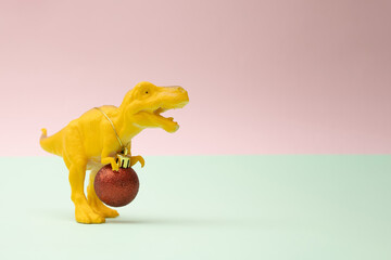 Yellow toy dinosaur tyrannosaurus rex with new year Christmas red baulbe around nack with golden...